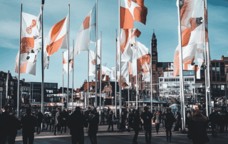 Drapeaux publicitaires flottant sur une place urbaine animée, avec foule et bâtiments en arrière-plan