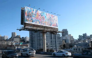 Panneau publicitaire géant coloré surélevé au-dessus d’une voie rapide urbaine avec voitures en circulation